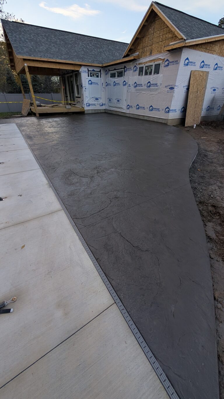 Charcoal slate-pattern stamped concrete pool deck surround viewed from yard toward a new construction home in Rochester NY