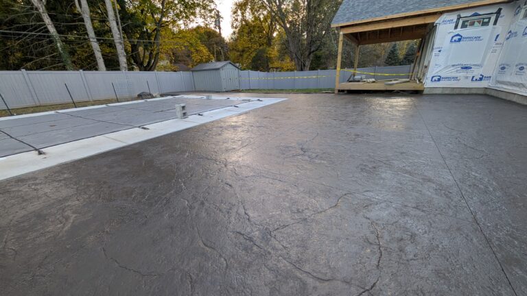 Wide view of large charcoal stamped concrete pool deck surrounding a covered in-ground pool at a new construction home in Rochester NY