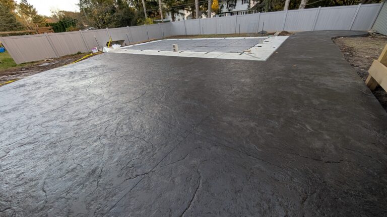 Alternate wide-angle view of dark charcoal stamped concrete pool deck surround with covered pool and vinyl privacy fence in Rochester NY