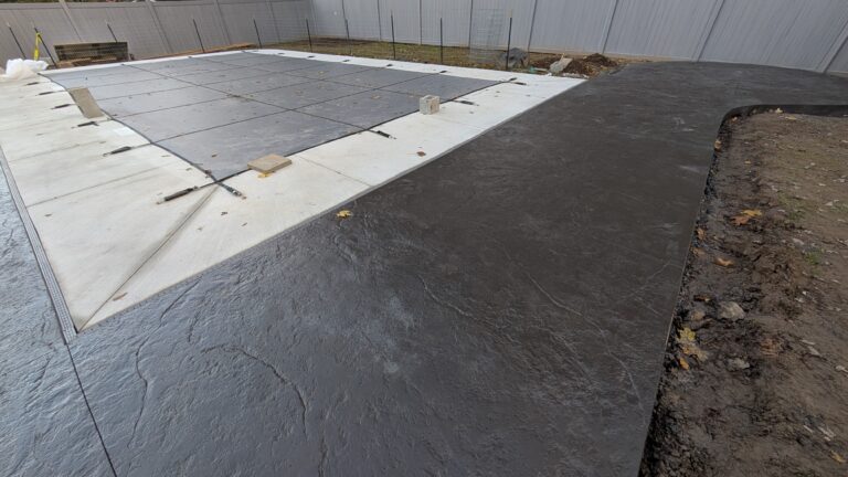 Close-up of dark charcoal slate-texture stamped concrete pool deck with curved edge beside a covered in-ground pool in Rochester NY
