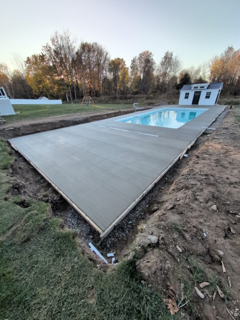 Smooth concrete pool deck surround around a freeform kidney-shaped in-ground pool with black aluminum fencing in Pittsford NY