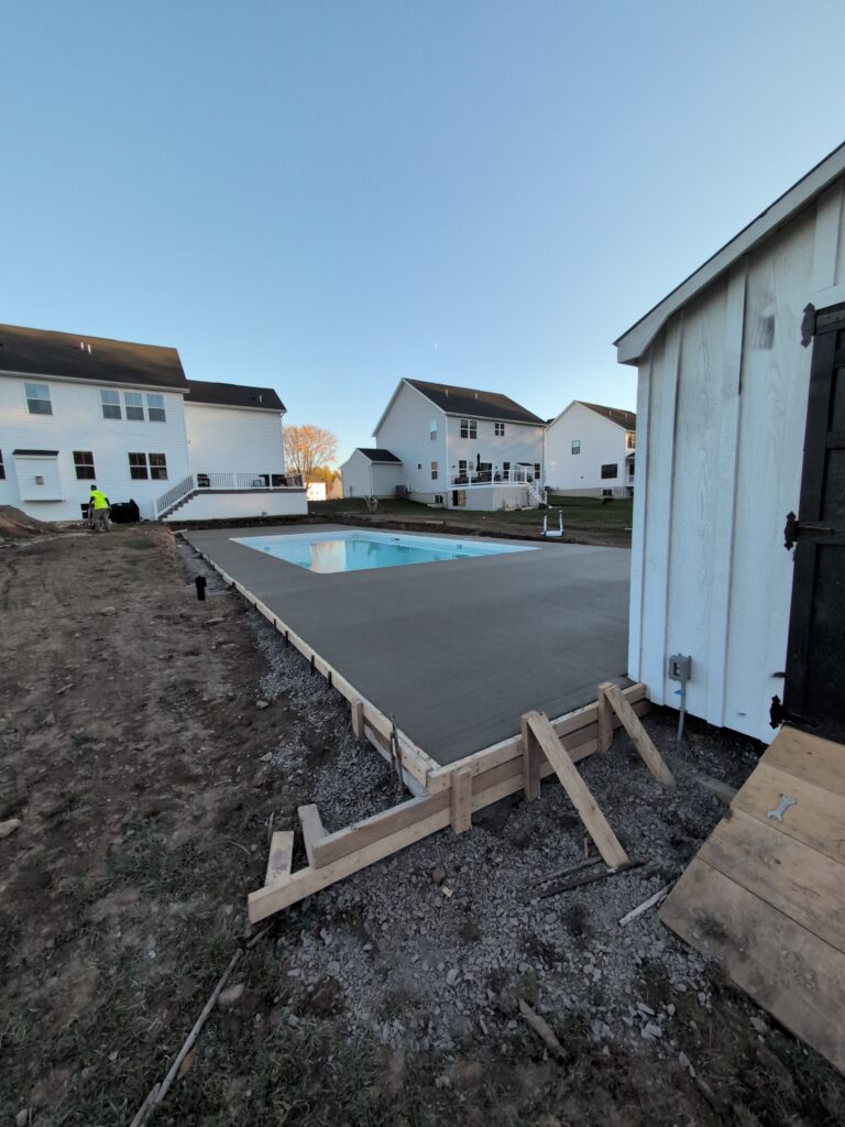Broomed concrete pool deck surround wrapping a covered in-ground pool at a new construction home in Penfield NY