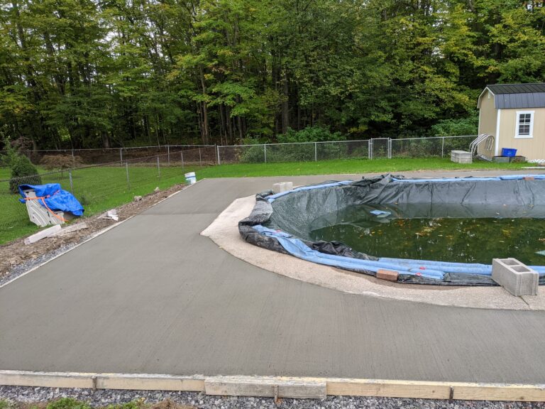 Freshly poured broomed concrete pool deck and patio surrounding a freeform in-ground pool with chain-link fence in Rochester NY