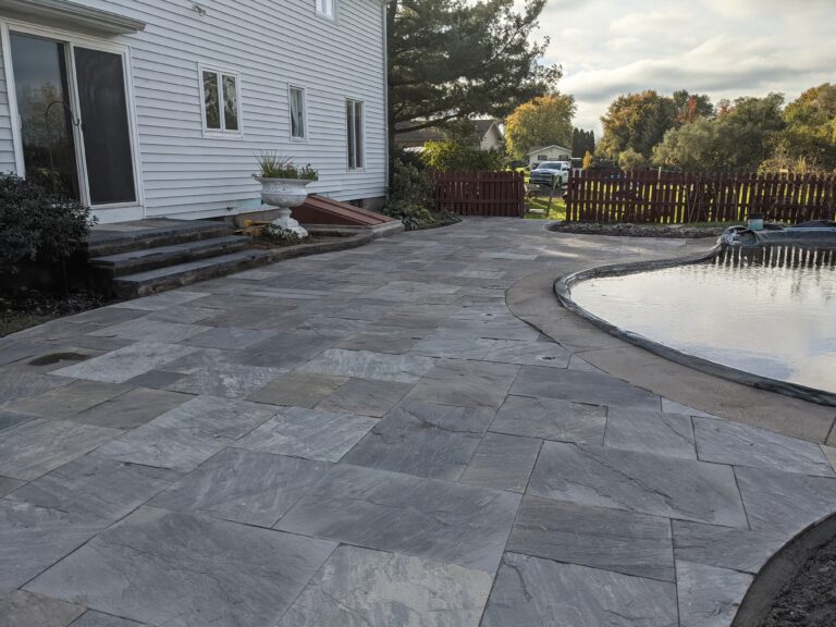 Completed natural stone tile patio surrounding covered in-ground pool with stone steps, Monroe County NY