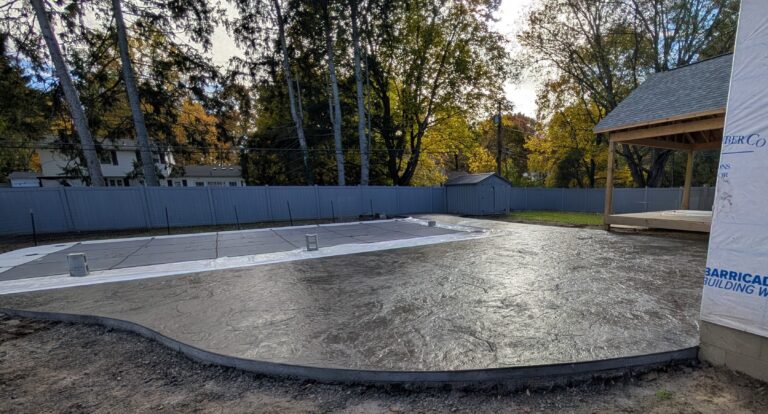New broomed concrete pool deck surround around a rectangular in-ground pool at a new construction home in Fairport NY at dusk