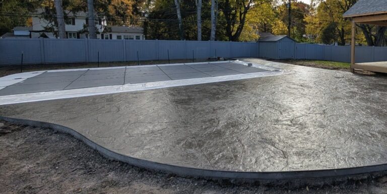 Dark stamped concrete pool deck surround around a covered in-ground pool with new covered porch and vinyl fencing in Fairport NY