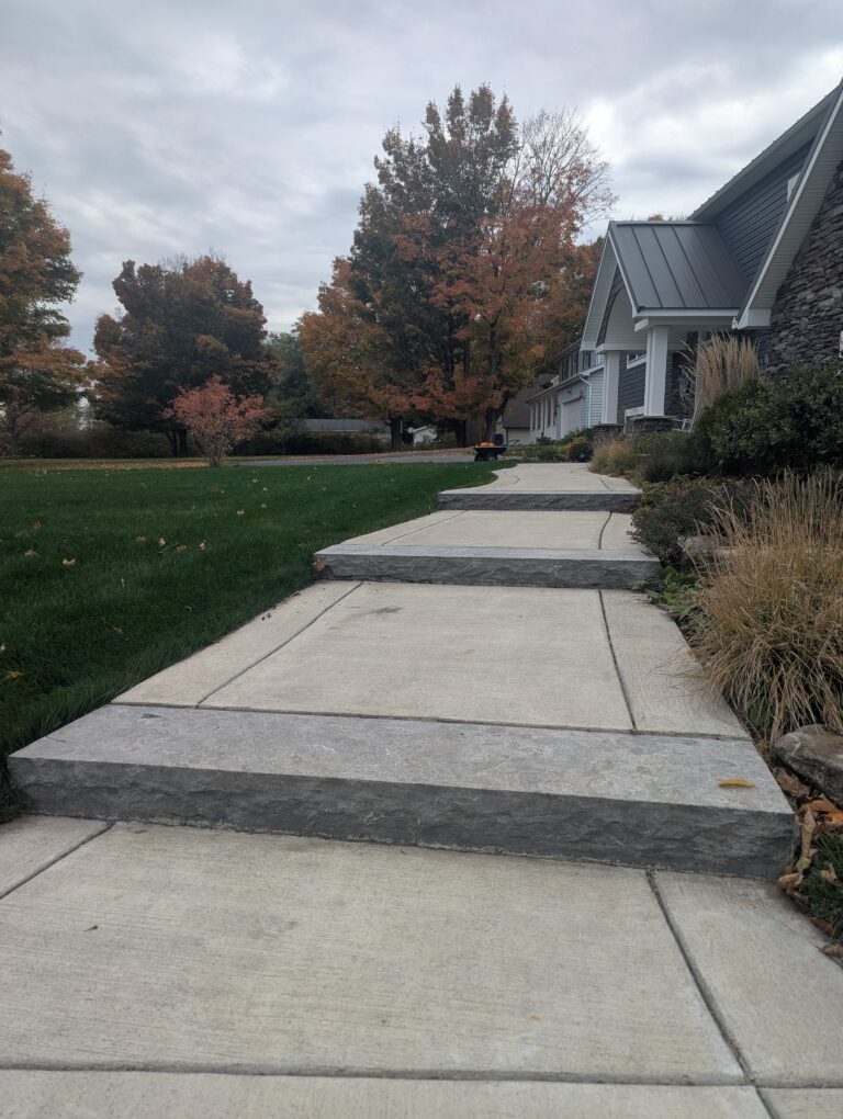 Long concrete sidewalk with rough-cut natural stone step edging beside residential home, Spencerport NY
