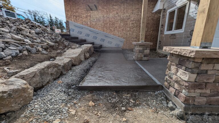 Stamped concrete patio under construction with natural stone veneer columns and boulder retaining wall, Rochester NY