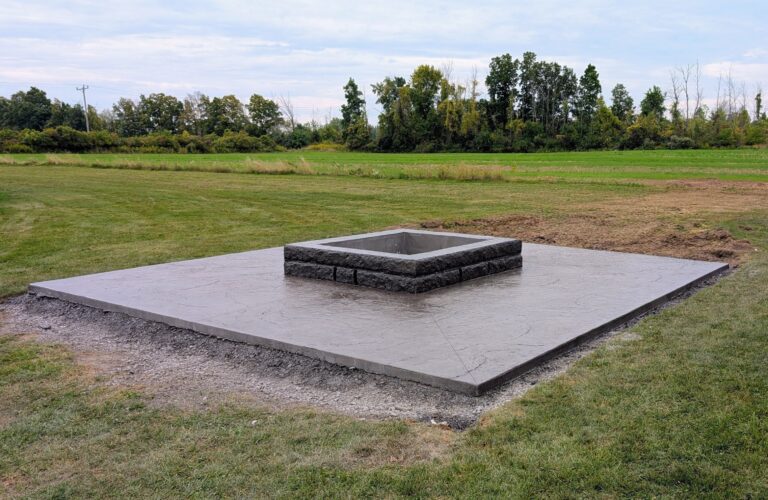 Wide view of stamped concrete fire pit patio with concrete block surround in rural yard – Brockport NY