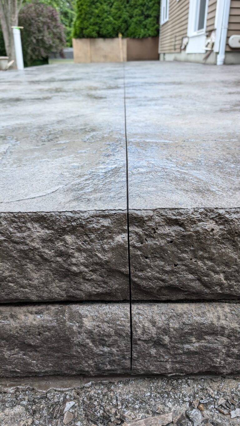 Close-up side view of elevated stamped concrete patio edge with chiseled stone-face riser – Rochester NY