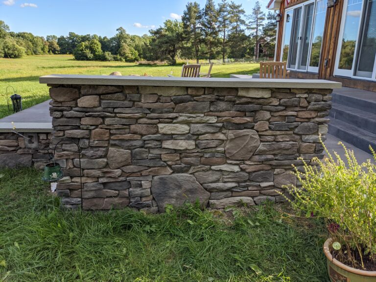 Close-up of fieldstone veneer patio knee wall with large irregular stones in brown and grey tones and concrete cap, Chili NY