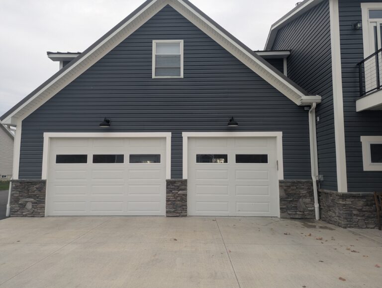 Concrete driveway apron in front of two-car garage with stone veneer base and blue siding in Rochester, NY